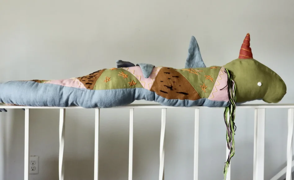 A textile artwork, Npisune’get (Provides Medicine), featuring Jipijka'm, a Mi'kmaw sea serpent, made with red, blue, black, and white fabric, embroidered with plants and symbols