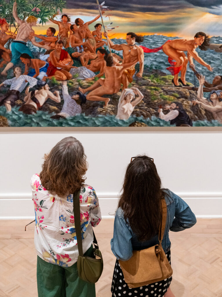 Installation view showing gallery visitors viewed from behind as they observe Kent Monkman's Study for mistikôsiwak (Wooden Boat People)—Welcoming the Newcomers (Final Variation) (2019).