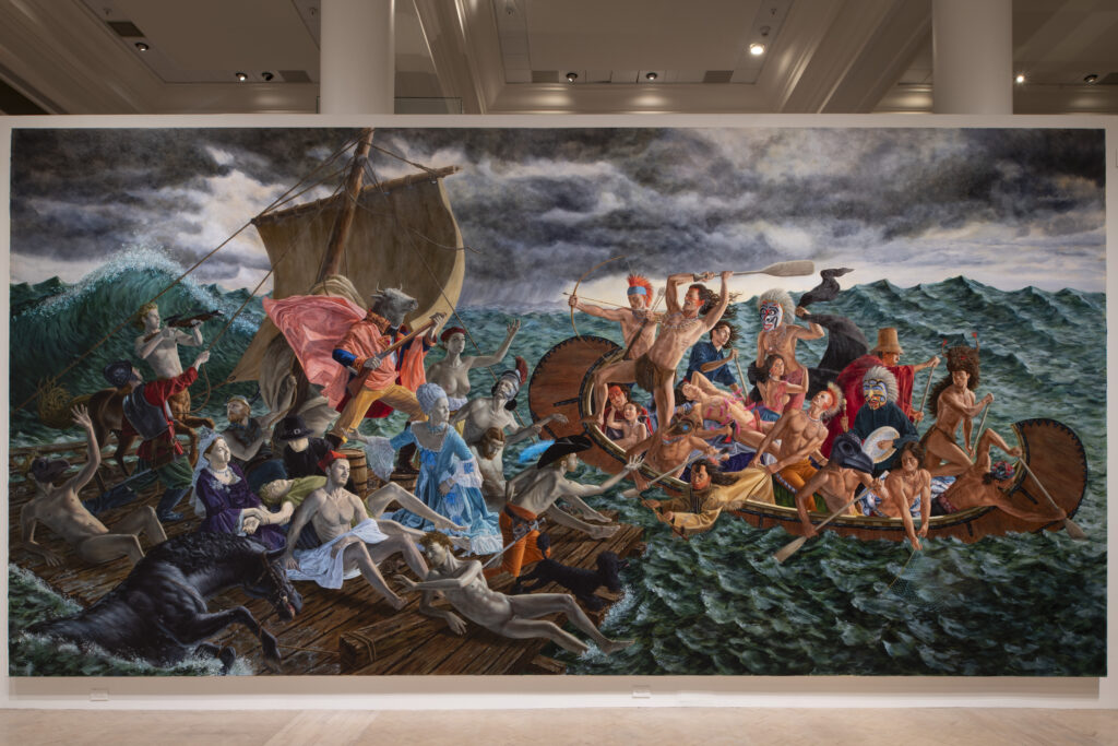 A massive, wide narrative painting installed on a white gallery wall depicting a dramatic scene at sea, with Indigenous figures in a wooden vessel on the right confronting European colonial figures and mythological creatures on a raft to the left under a dark, stormy sky.