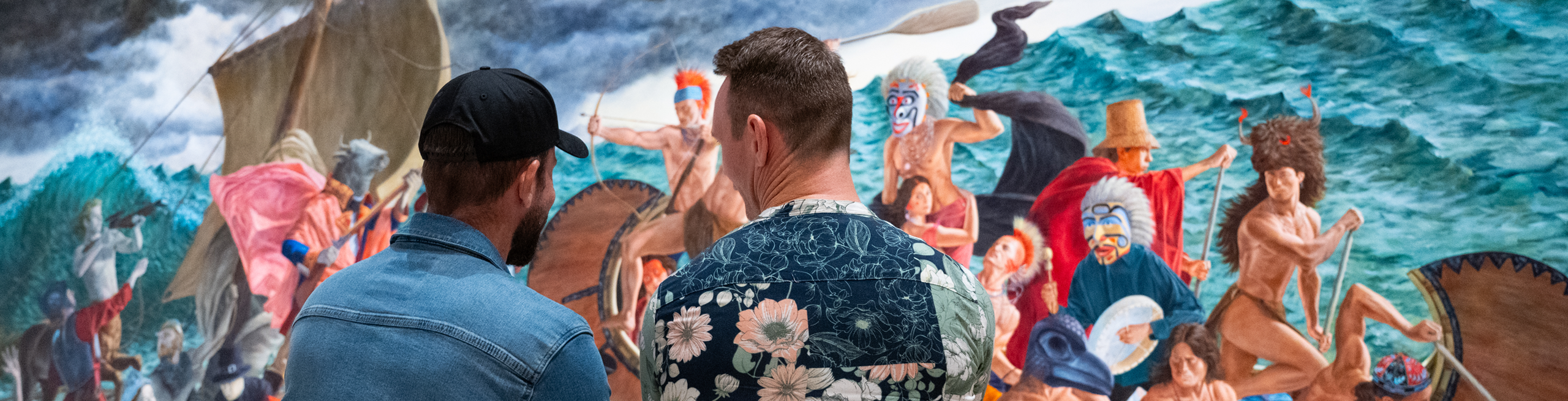 Installation view of Kent Monkman: Breaking Waves, showing two people viewed from behind looking closely at a large, vibrant painting of figures navigating stormy ocean waters in traditional boats.