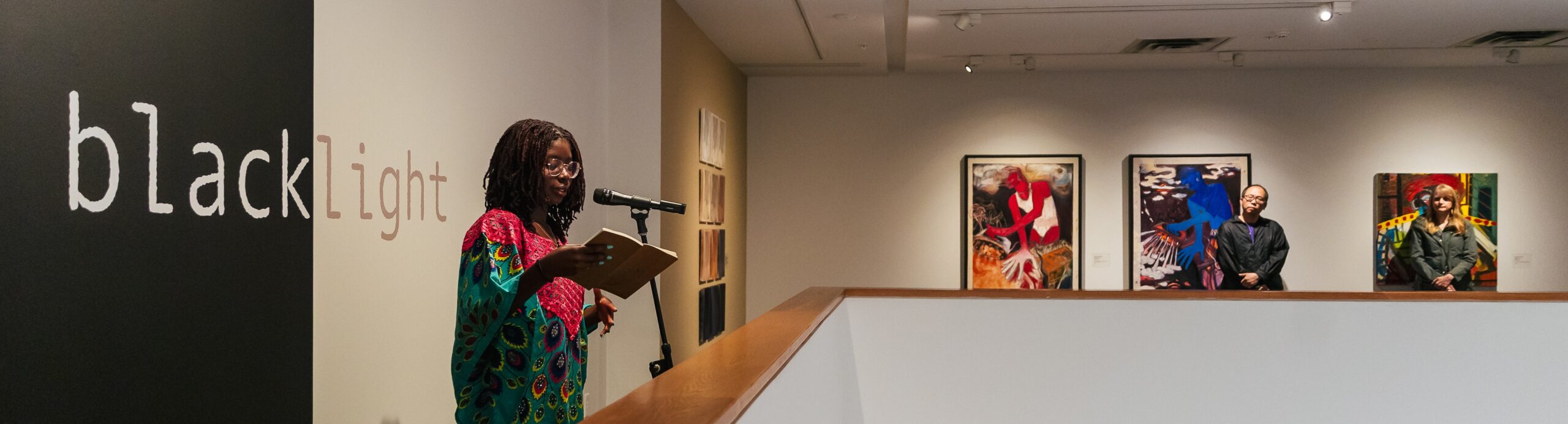 A Black woman reads from a book standing at a microphone